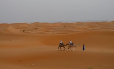 Two people riding camels in a vast desert landscape.