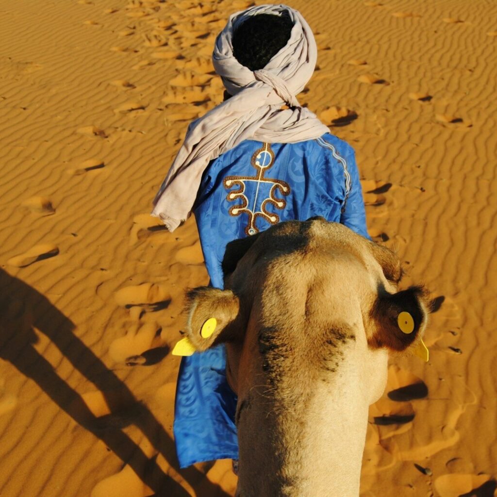 a man in a blue robe walking a camel in the desert